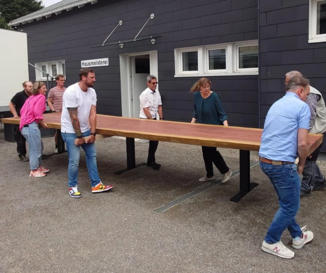 Das Team trägt den Monolith Tisch an seinen Platz in der Ausstellung. 