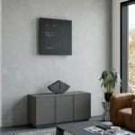 QLOCKTWO Earth 90 Black Pepper, Wanduhr an grauer Wand pber Kommode