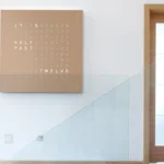 QLOCKTWO Earth 90 Hazelnut, Wanduhr an weißer Wand