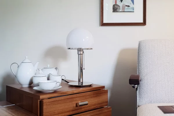 Tecnolumen Wagenfeldleuchte WA 24 Tecnolumen Wagenfeldleuchte WA 24, mit Metallfuß, neben einem Kaffeegeschirr